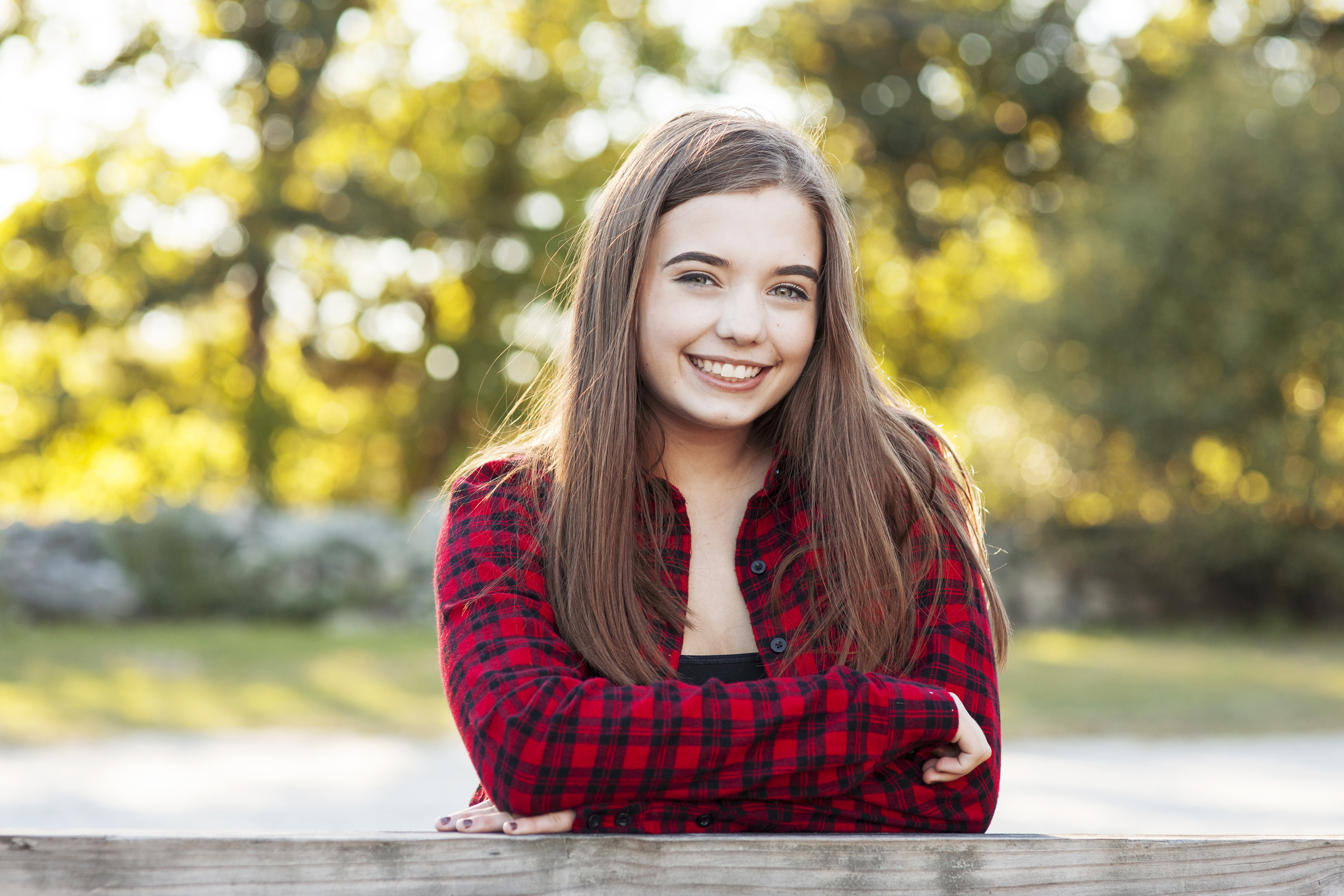 senior girl in plaid shirt leans on fence with fall colors