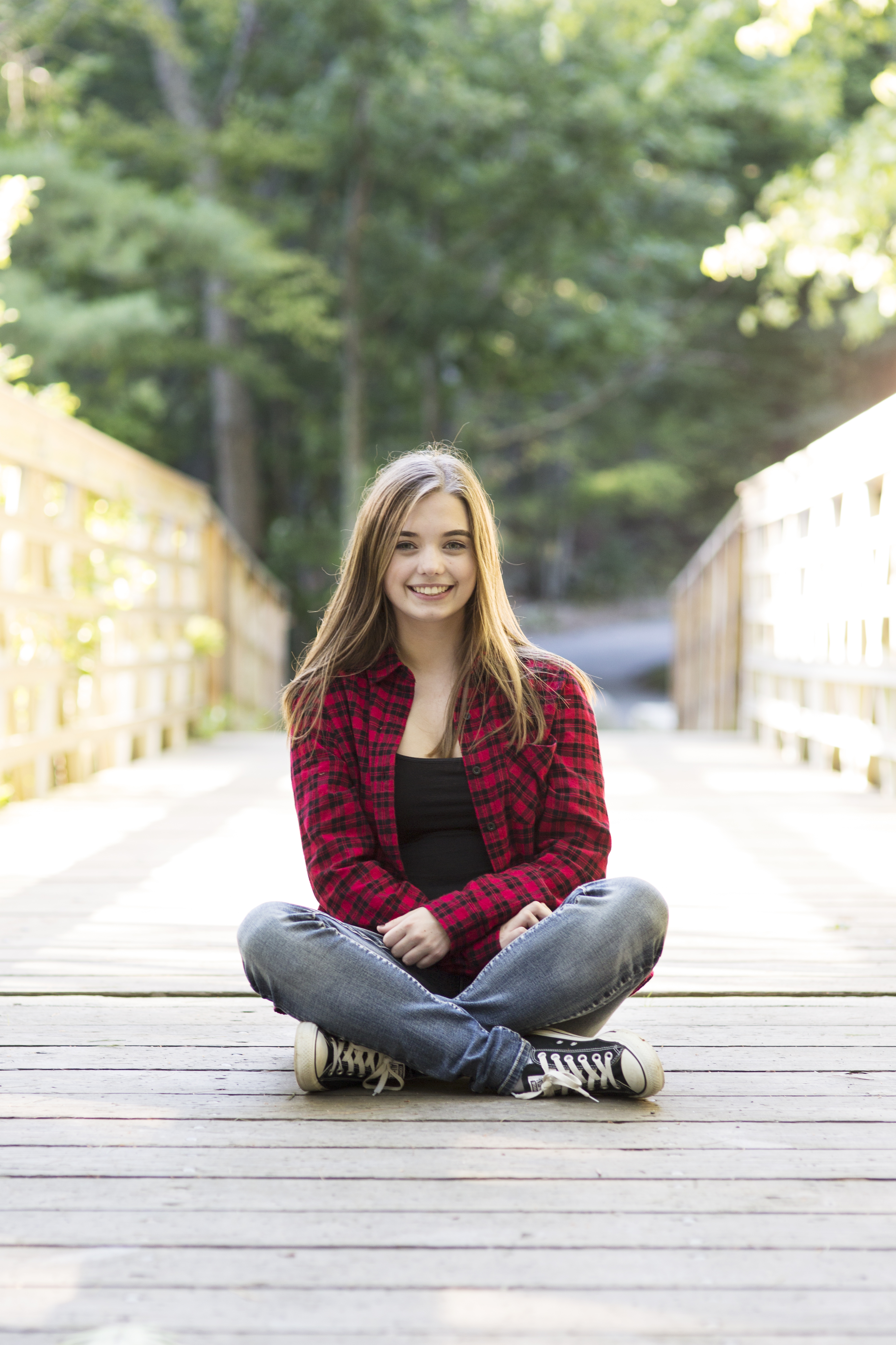 senior girl sitting on sunlit bridge in the woods