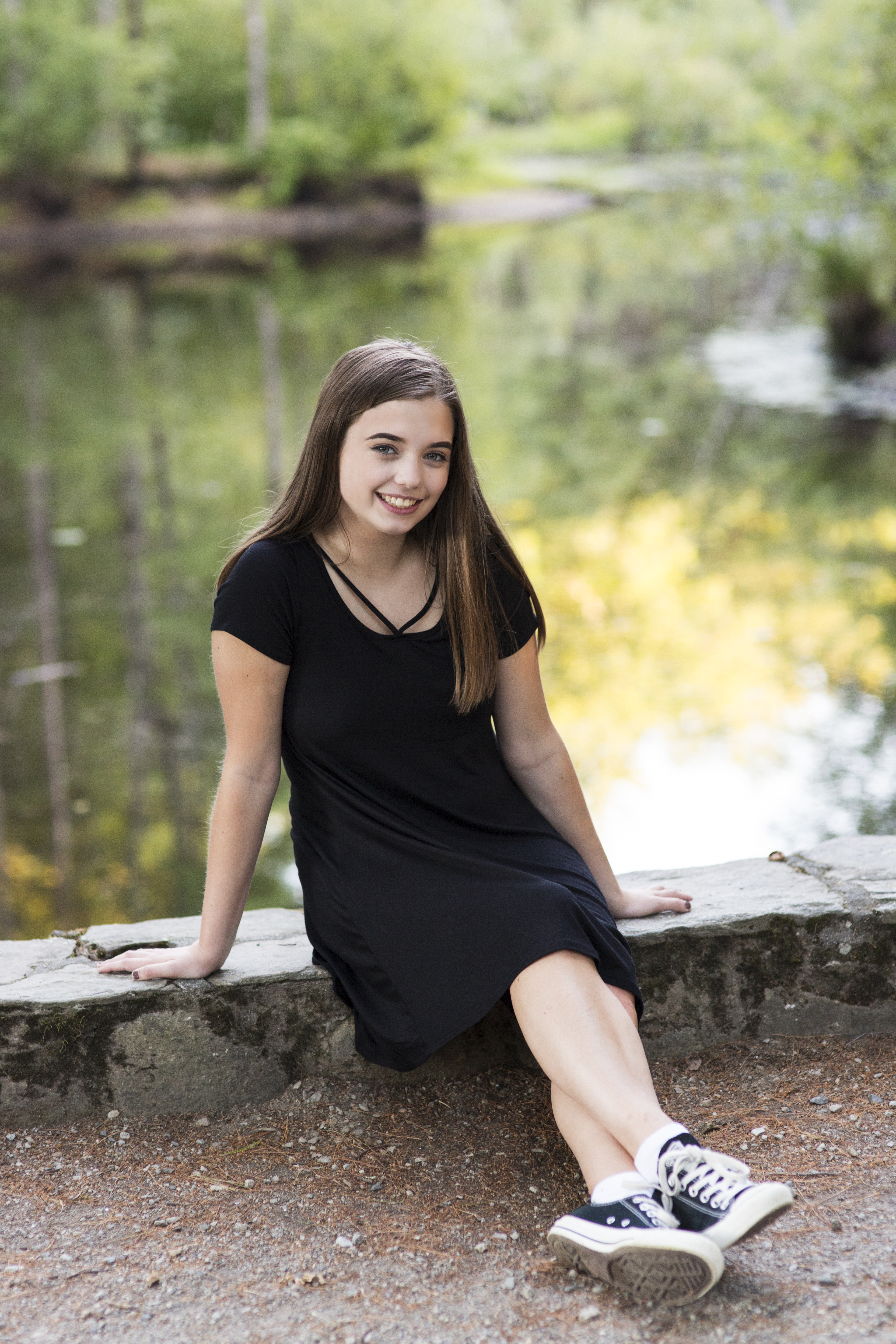 Senior portrait of girl in black dress on stone wall by water