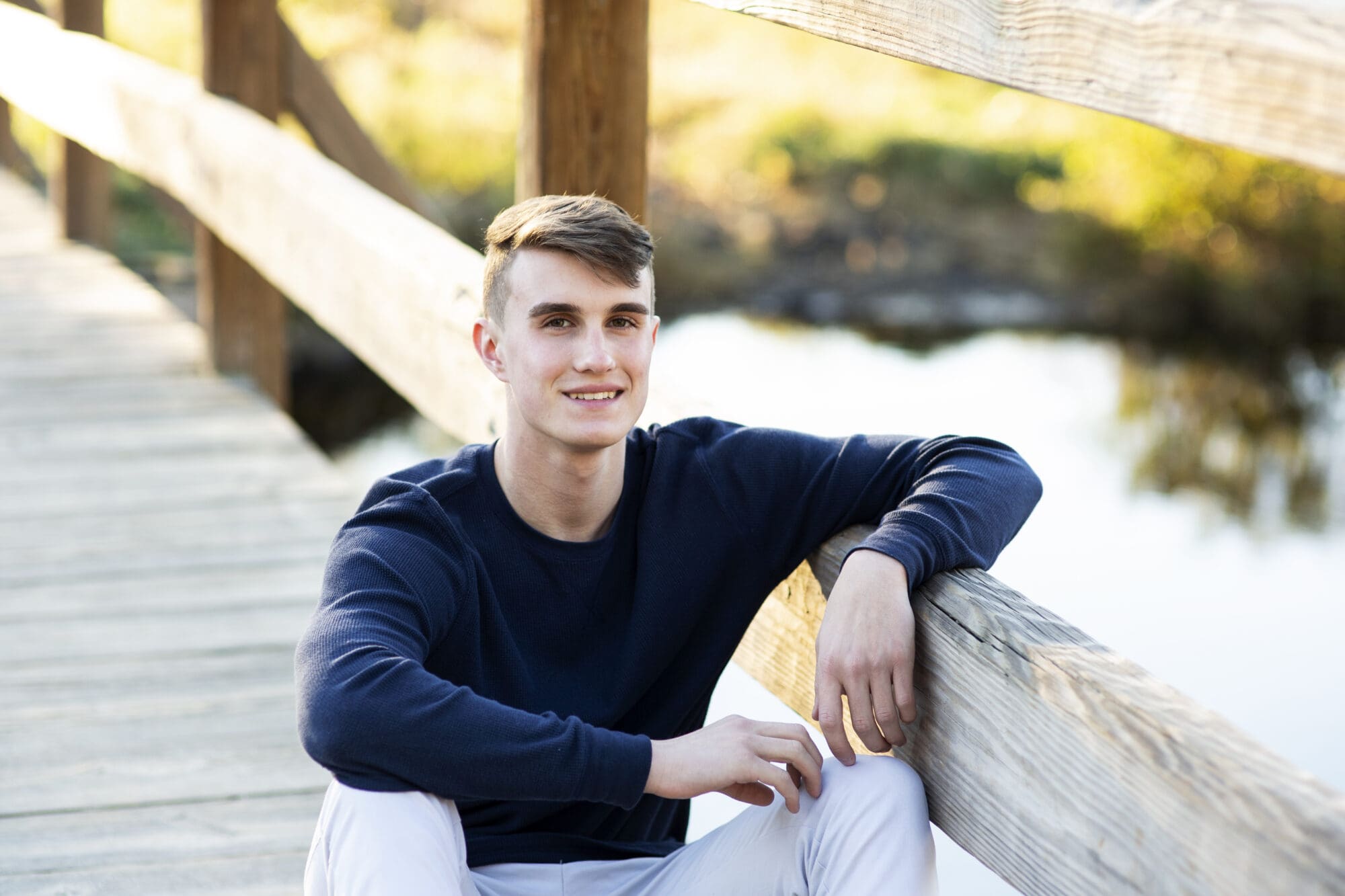 senior boy photo sitting on wooden bridge over the water