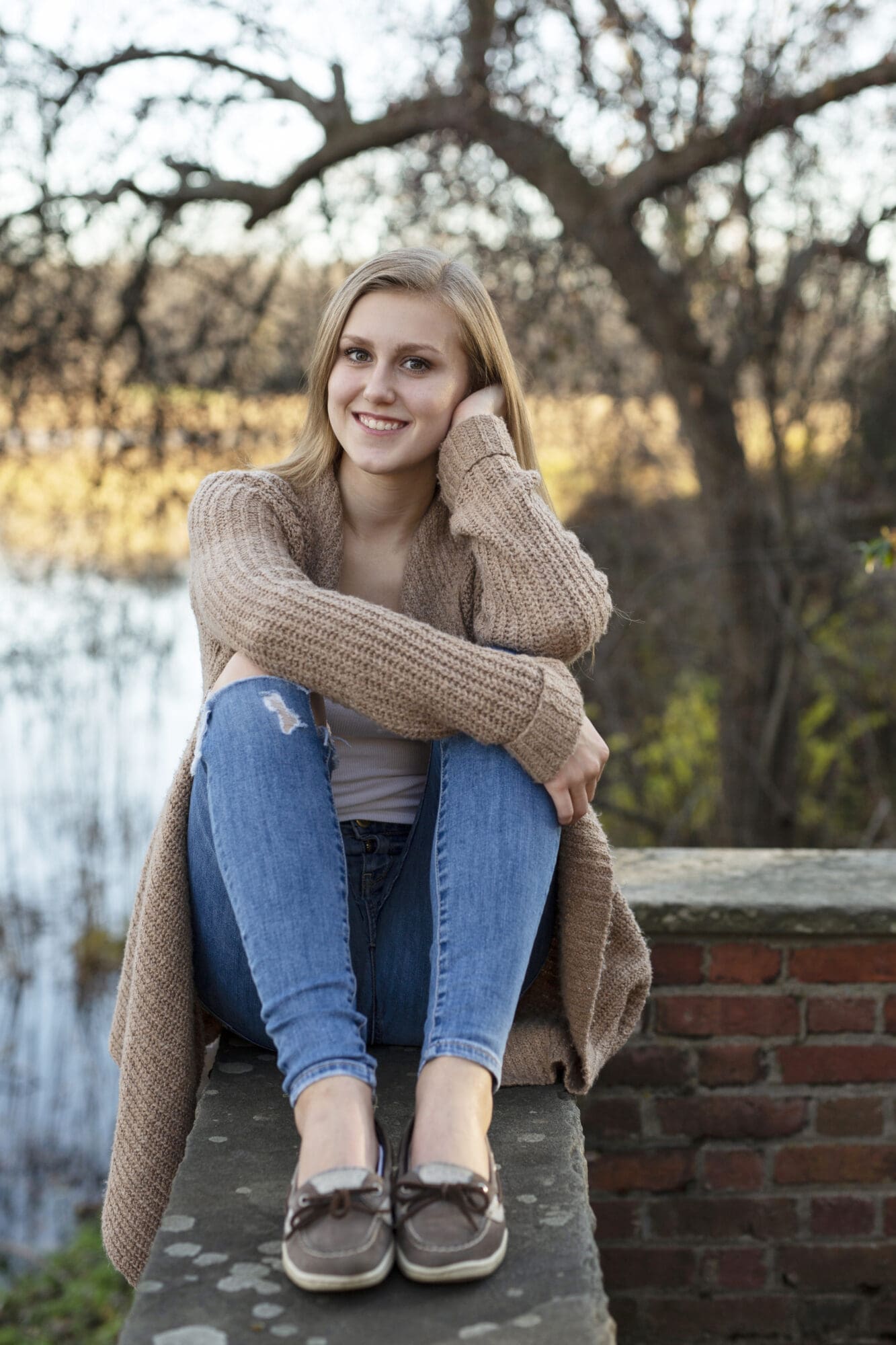 senior girl sitting on brick wall with elbows and knees bent