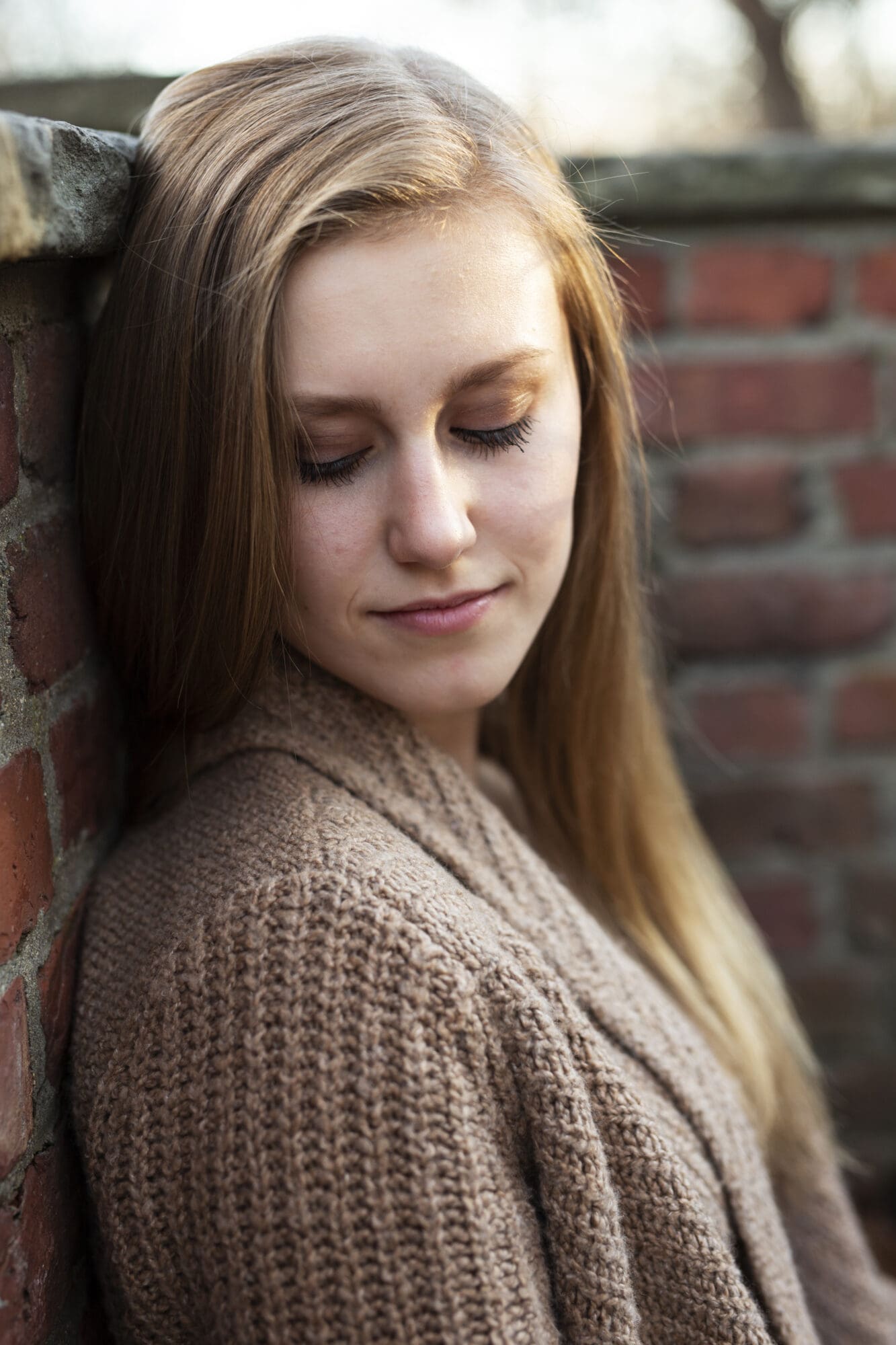 serious girl senior portrait looking down over her shoulder by brick wall
