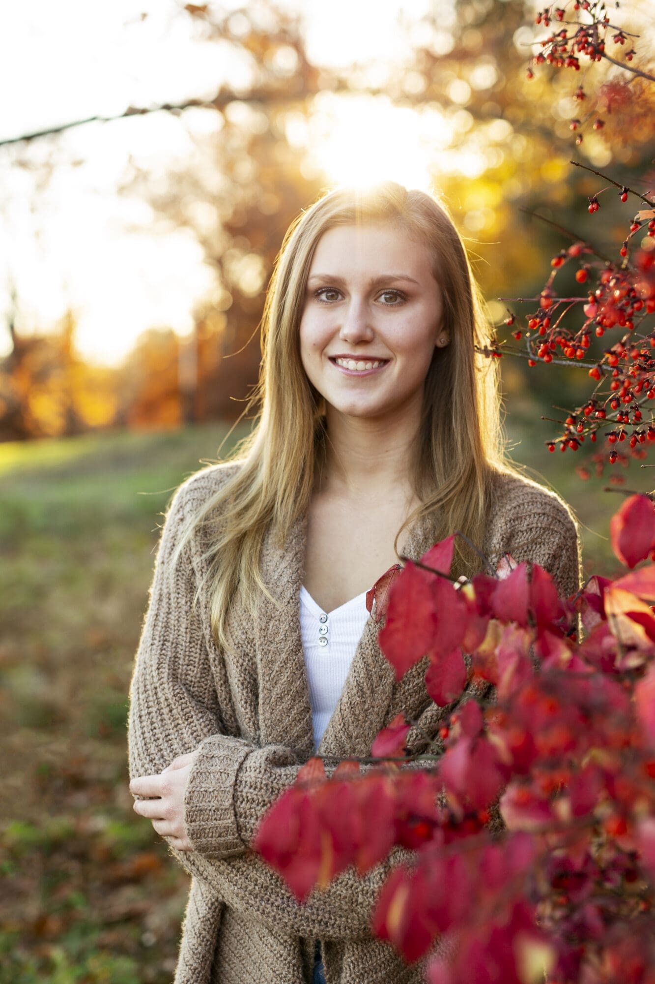 girl senior photo with red leaves and berries and sun flare at golden hour