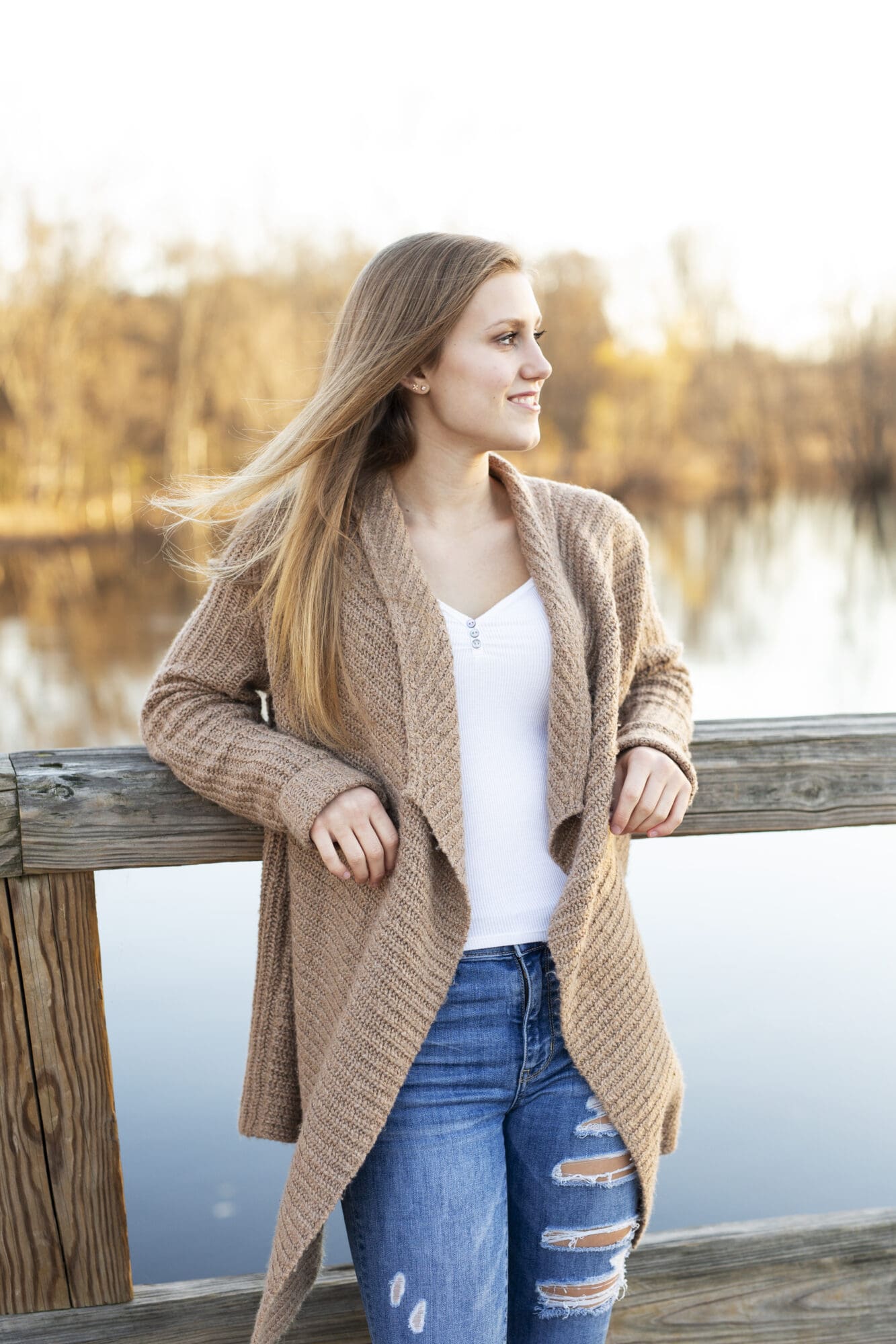 senior girl leans on wooden bridge looking over her shoulder with hair blowing in the wind